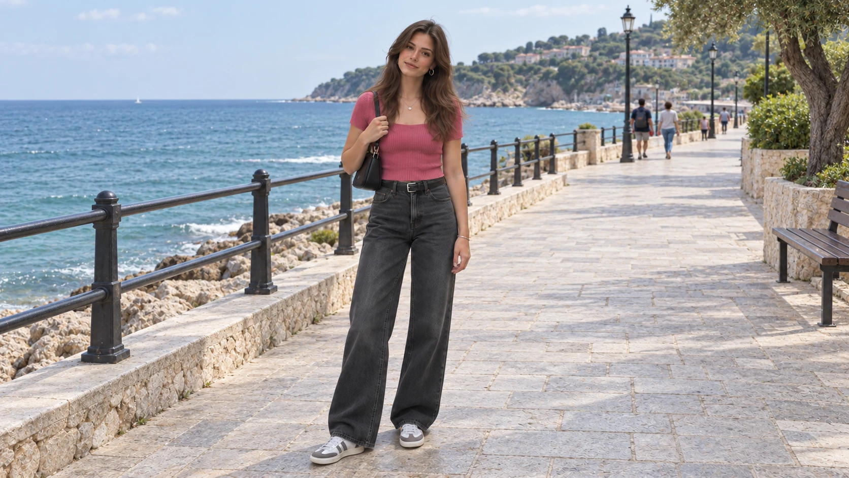 The same woman in her rose-pink top and charcoal jeans on a sunny seaside promenade.